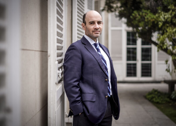 Abogado en traje formal posando en exterior de edificio institucional.